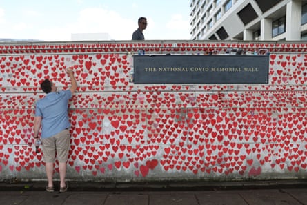 A man writes the name of a relative who died of Covid on a wall covered with small red painted hearts bearing the names of victims.