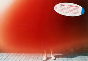 An overexposed photo showing only a pair of feet beneath a blur of red, with a "Quality Control" advice sticker on top