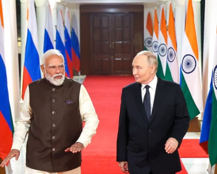 Modi and Putin walk down a corridor lined with a red carpet. Either side are rows of Russian and Indian flags