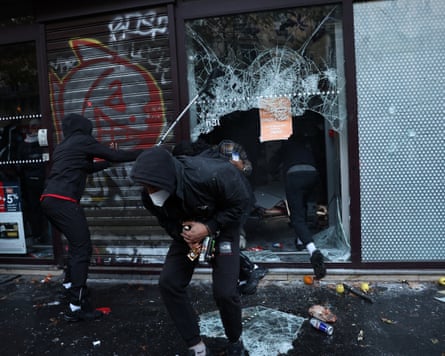 Hooded protesters smash a shop’s shattered glass window during clashes in Paris