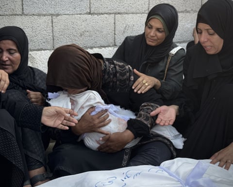 Women with black headscarves holding a tiny shroud.