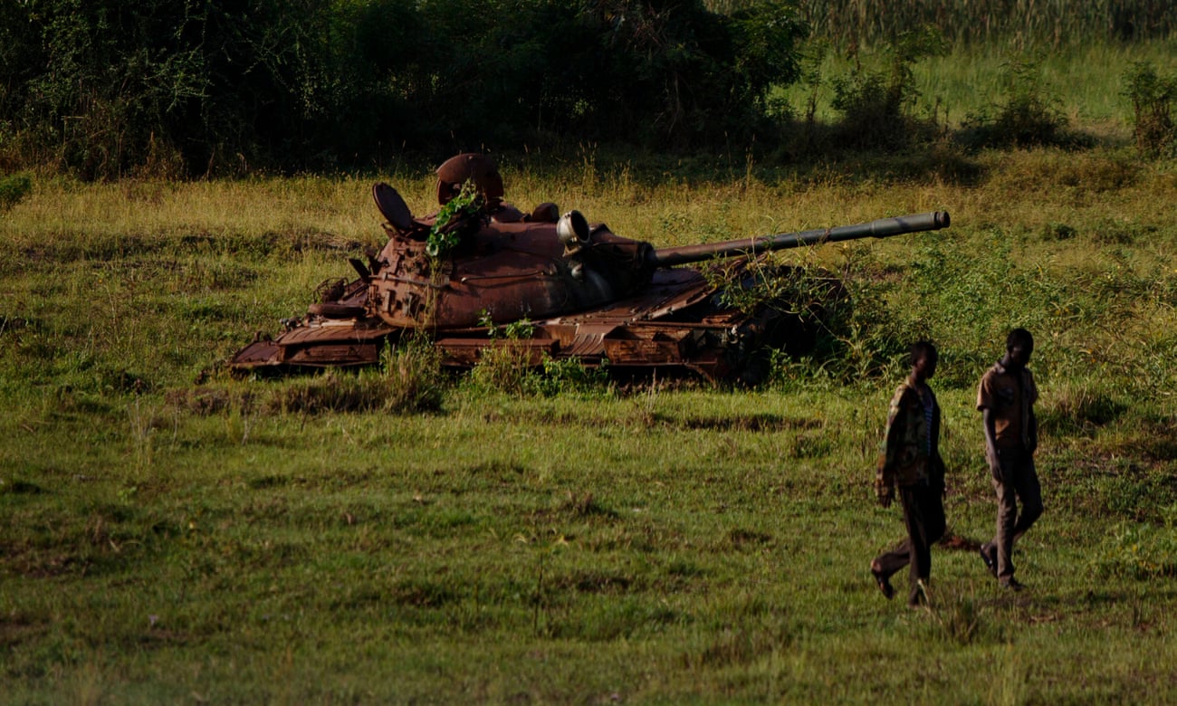Two South Sudanese government soldiers walk past a disused tank in Bentiu, South Sudan