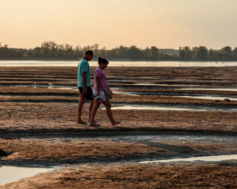 People walk on the exposed riverbed of the Danube River in Dunaszentbenedek, Hungary.