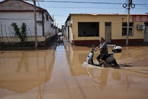 A man attempts to drive an electric moped through a flooded street in the town of Taishitun, in the district of Miyun.