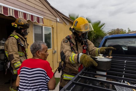 Firefighters speak to a woman, one firefighter holds a cooking pot