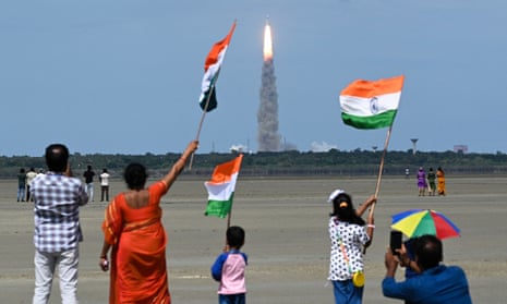 People wave Indian flags as an Indian Space Research Organisation rocket carrying the Chandrayaan-3 spacecraft lifts off on 14 July.