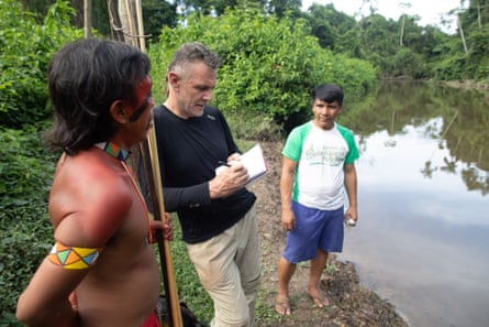 Three men talk by a river in the Amazon rainforest
