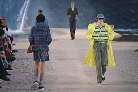 Models in shorts and a raincoat on the catwalk covered in sand