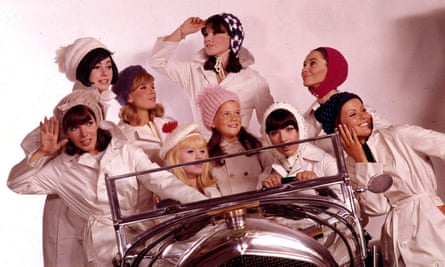 A group of young women wearing white coats, hats and bonnets as they crowd around a car in 1965