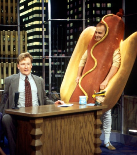 man in hot dog costume next to conan behind desk