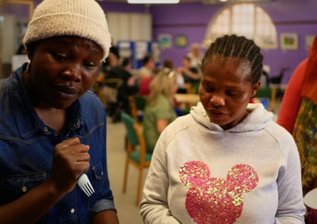 Two women holding cutlery, with people seated at tables in the background