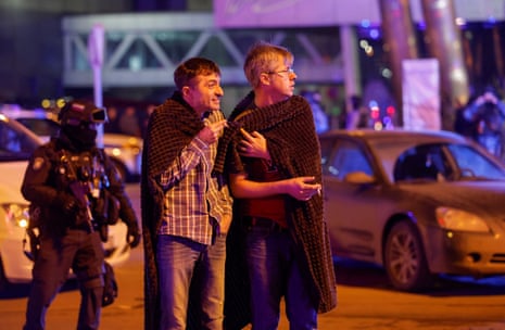 Men cover themselves with blankets as a Russian law enforcement officer stands guard near the burning Crocus City Hall concert venue following a reported shooting incident, outside Moscow, Russia, March 22, 2024.