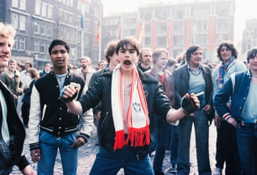 Queens Day, Dam, Amsterdam, 1980. A young man raises his arms, mouth agape at the centre of a large group of other men