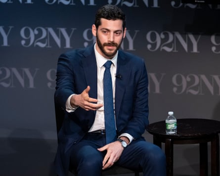 Man seated in suit gesture and speaks.