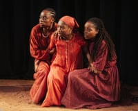 Three young women of colour huddled together on dark stage