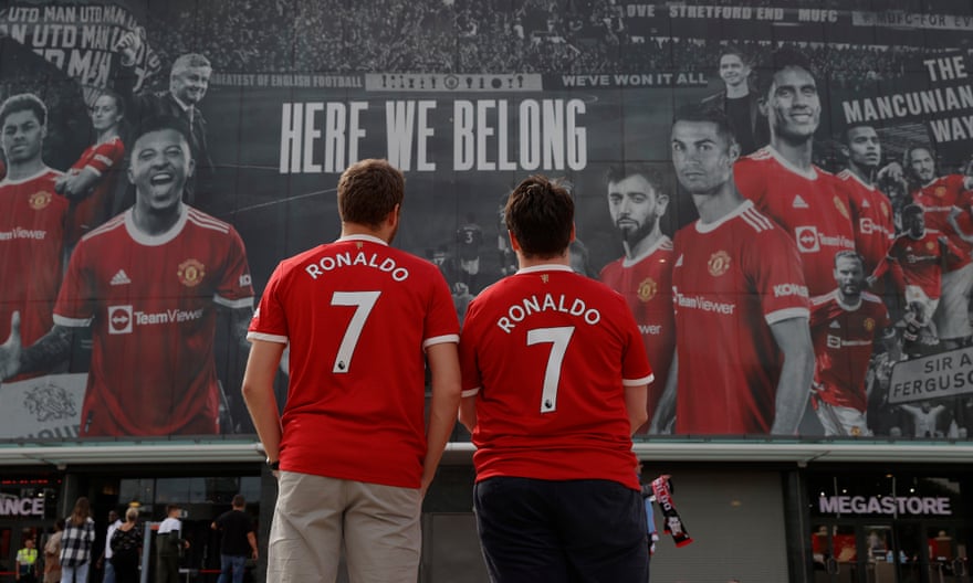 Two Manchester United fans wearing freshly bought Cristiano Ronaldo shirts look at the huge banner on the front of the stadium the day before his return match against Newcastle