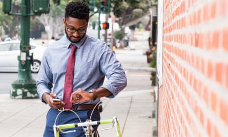 Young man standing beside bicycle, using smartphone, looking at wristwatch