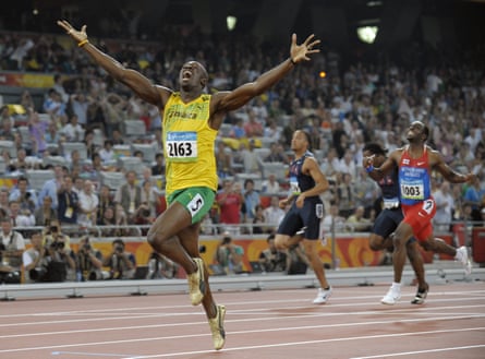 A tall black man stretches out his arms as he runs ahead of two other black athletes on a track