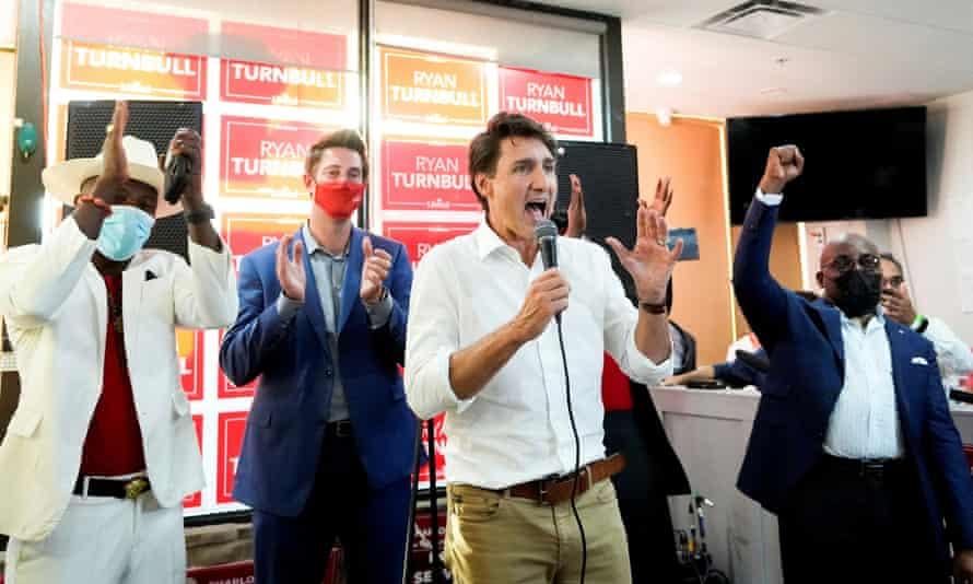 Justin Trudeau speaking animatedly at an event with other people on the podium applauding.