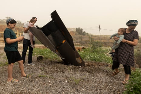A family of five with small children stand near a missile lodged in the ground.