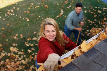 A woman stands atop a ladder clearing her roof gutters