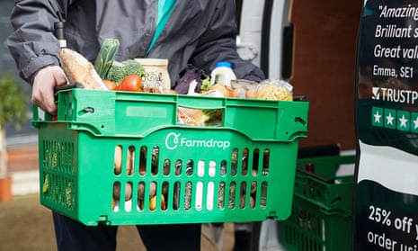 A Farmdrop worker carries a green branded crate of groceries beside a delivery van