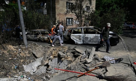 People in Kyiv walk near cars damaged by fragments of a downed Russian Kamikaze drone.