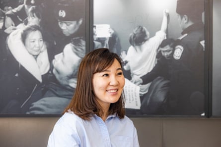 A young Mongolian woman smiles in front of a series of large black and white news photos hung on the wall