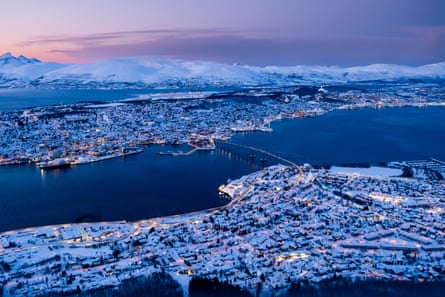 Aerial view s nowy city lit up at twilight with a bridge acrsoss a harbour and mountains on a polar night