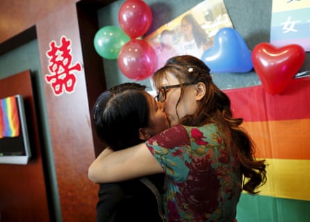 Two people kiss in front of a rainbow banner with balloons on it