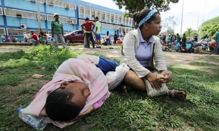 People lie on the grass outside a San Felix health centre, waiting for malaria treatment
