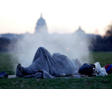 A homeless man in a blanket lying on the National Mall with the US Capitol building in the background