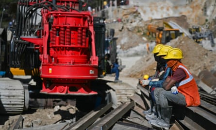 Rescue personnel sit beside machines near the mouth of the tunnel