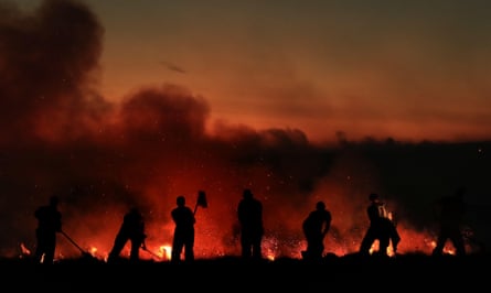 A line of men with firebeaters silhouetted against a fire at sundown 