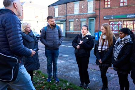 A young woman speaks as people stand around her on a street, including two schoolgirls