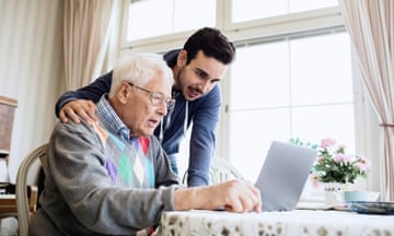 A young man helps an older man use a laptop.