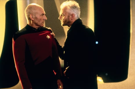 Captain Picard and Dr Soran stand close in profile, one gripping the other's shoulder