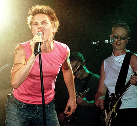 Mel C wearing jeans and a pink top, on stage with a woman in a white top playing guitar behind her