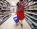 A shopper walks down a supermarket aisle carrying a basket with fruit and veg either side of her