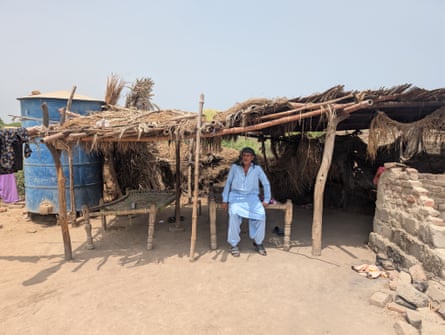 A man sits in the shade of a wooden shelter in a rural village in Pakistan.