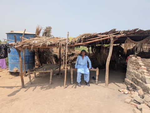 A man sits in the shade of a wooden shelter in a rural village in Pakistan.