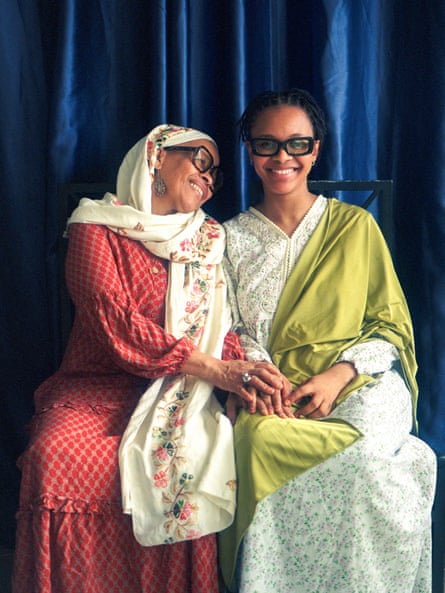 a mother and daughter wearing colorful dresses, shawls and chunky glasses smile and pose for a portrait