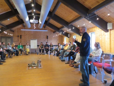 A hall with chairs ringing the outside, many occupied by members of the Interspecies Council; one member, standing up, is leading the discussion