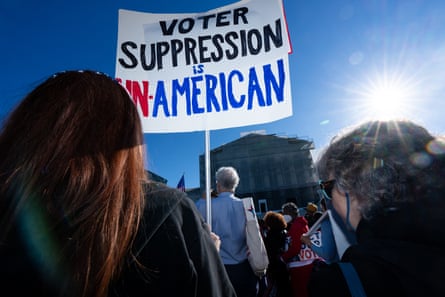 A person in a crowd holding a sign that says 'Voter Suppression is Un-American.'