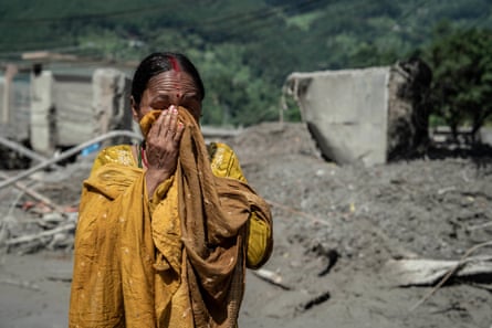 A woman holds her hands to her face among the mud-covered ruins of buildings