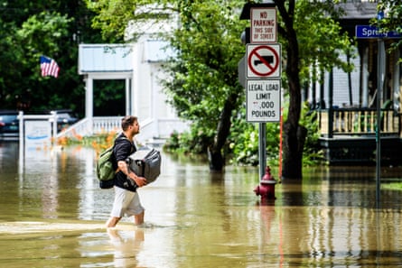 A man carries a suitcase to higher ground, wading through the overflowed Winooski River in Vermont.