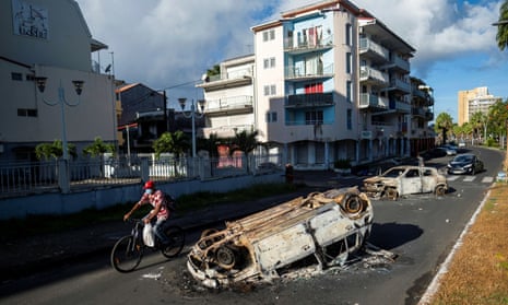 A man rides his bicycle past burnt cars after violent protests in Pointe-à-Pitre, Guadeloupe.