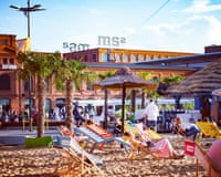 At Manufaktura in Łódź, people relax on colorful deck chairs under umbrellas on an urban sand beach