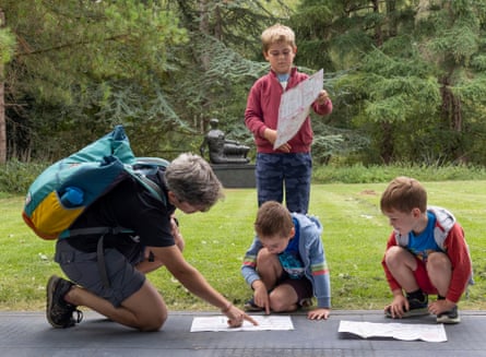 An adult and three kids pore over maps with a reclining sculpture behind