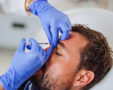 gloved hands administering an injection into a man’s forehead